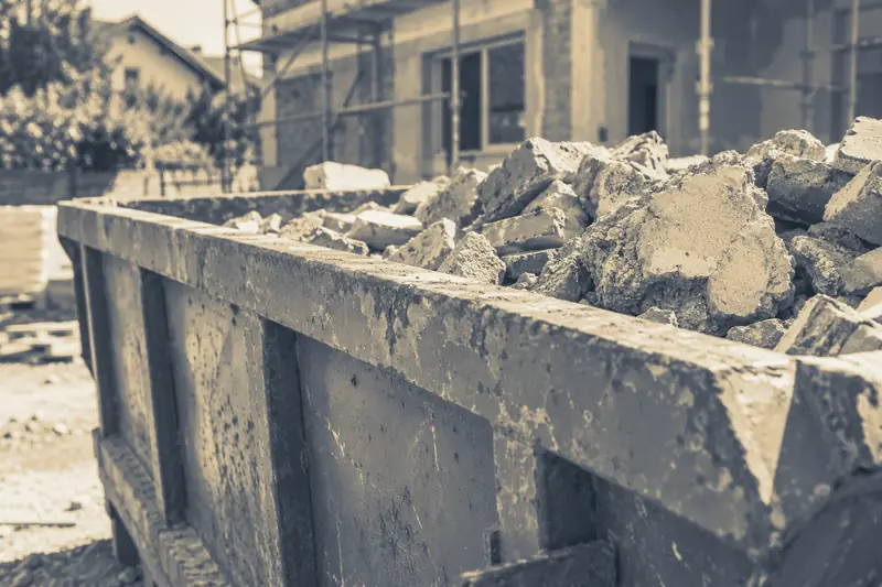 Briques et morceaux de béton dans une benne devant une maison en rénovation, image d’illustration
