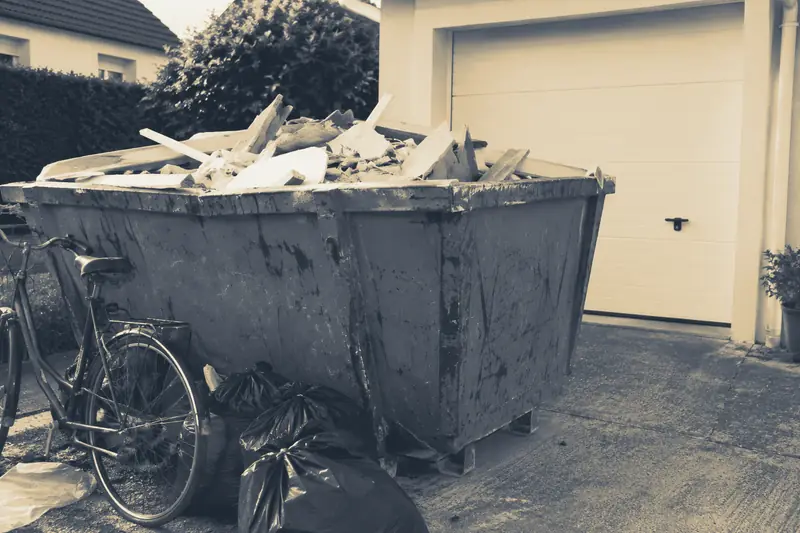 Une benne attend devant le garage d’une maison individuelle, image d’illustration