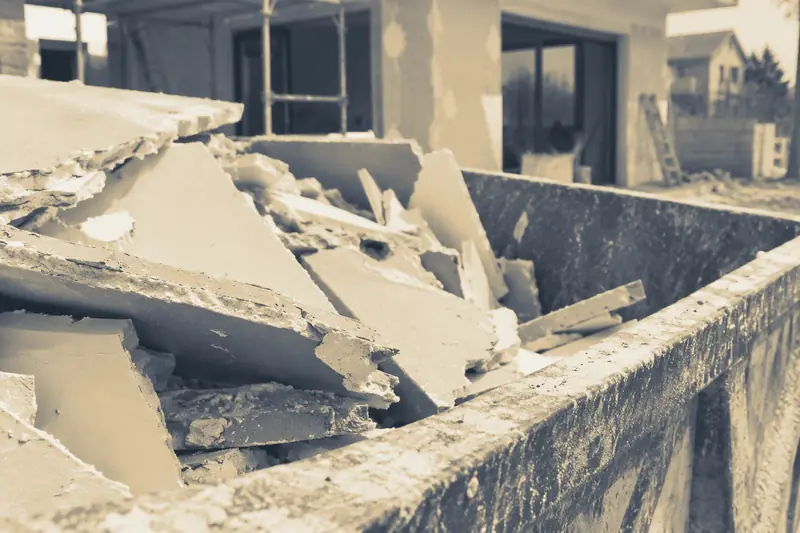 Plaques de plâtre cassées dans une benne devant une maison en chantier, image d’illustration