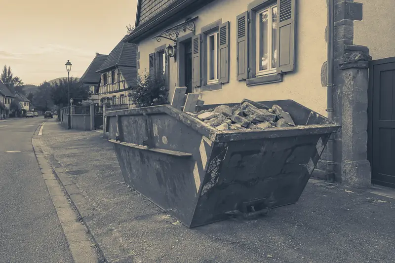 Briques et planches dans une benne au bord d’une rue de village, image d’illustration